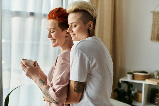 Dos mujeres con el pelo corto abrazándose apasionadamente delante de una ventana, mostrando su amor y conexión en un ambiente acogedor dormitorio. - Foto, imagen