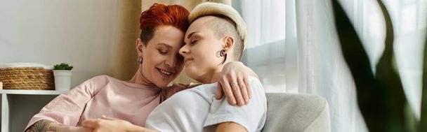 Zwei Menschen, ein lesbisches Paar mit kurzen Haaren, umarmen sich liebevoll auf einer gemütlichen Couch in einem warmen Wohnzimmer. - Foto, Bild