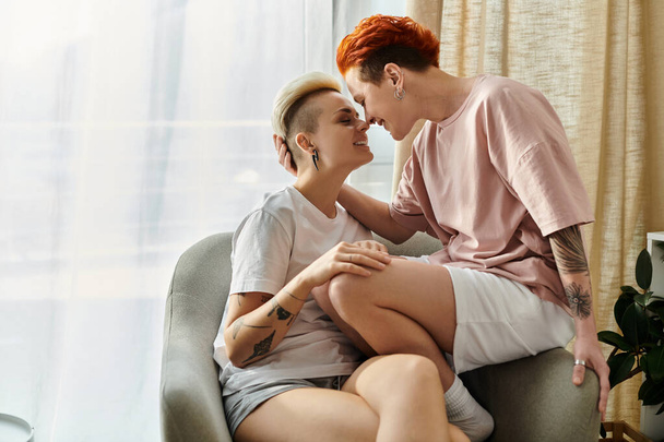 Due persone, una coppia lesbica con i capelli corti, si siedono su una sedia e condividono un bacio in un momento intimo. - Foto, immagini