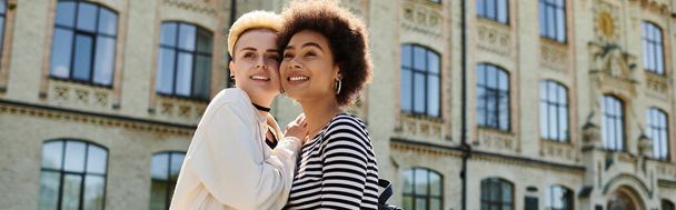 Due giovani donne alla moda, una coppia lesbica multiculturale, in posa davanti a un edificio universitario. - Foto, immagini