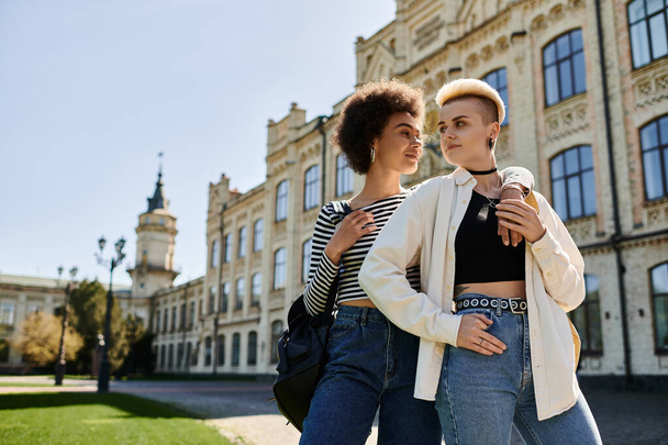 Dvě mladé ženy, multikulturní lesbický pár, elegantně pózují před starou budovou univerzitního kampusu. - Fotografie, Obrázek