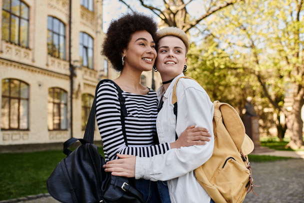 Dos mujeres jóvenes, una pareja lesbiana multicultural, abrazándose frente a un edificio en un campus universitario. - Foto, imagen