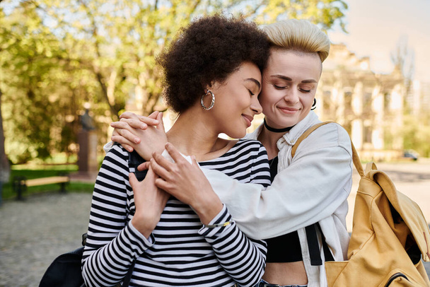 Νεαρό πολυπολιτισμικό λεσβιακό ζευγάρι μοιράζεται μια εγκάρδια αγκαλιά σε ένα όμορφο σκηνικό πάρκου. - Φωτογραφία, εικόνα