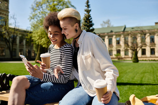 Due giovani donne sedute su una panchina, assorte nei loro telefoni cellulari. - Foto, immagini