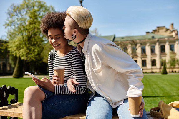 Two young women in stylish attire are seated on a park bench, deep in conversation, surrounded by greenery. - Photo, Image