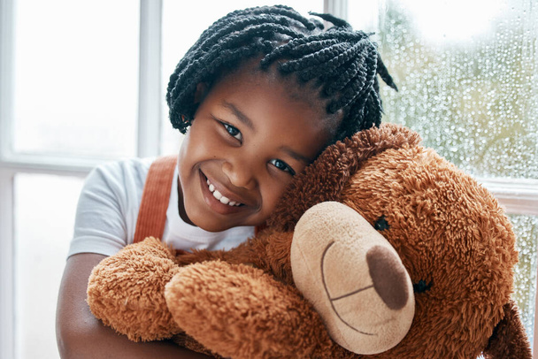 Black girl, portrait and teddy bear in house by window for happy, wellness and playing with toys. Homeless child, smile and stuffed animal in orphanage or children home for love, friendship and hug. - Photo, Image