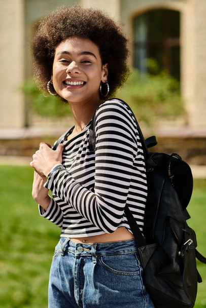 Een jonge Afro-Amerikaanse vrouw in een gestreept t-shirt en jeans loopt vol vertrouwen met een rugzak. - Foto, afbeelding