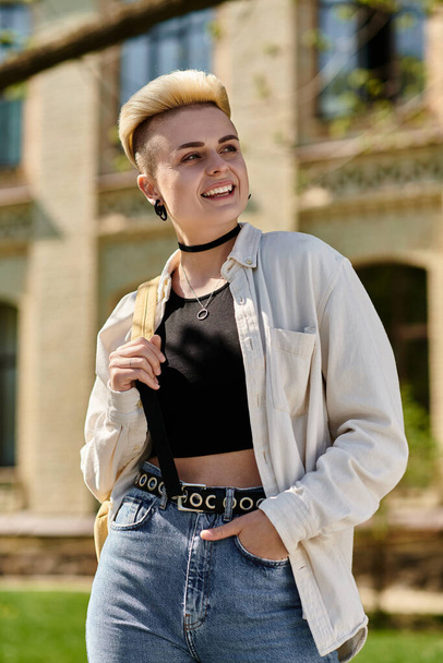 Young woman confidently struts in jeans and a t-shirt, showcasing her shaved head outdoors on a university campus. - Photo, Image