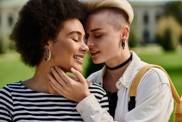 Um casal lésbico multicultural em trajes elegantes compartilha um abraço caloroso em um parque sereno perto de um campus universitário. - Foto, Imagem