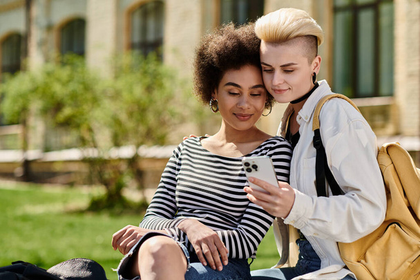 coppia lesbica in abiti casual sedersi sull'erba, assorto nel telefono, chiacchierare e condividere momenti. - Foto, immagini