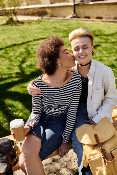 Zwei junge Mädchen teilen einen liebevollen Kuss auf einer Parkbank, umgeben von der friedlichen Atmosphäre der Natur. - Foto, Bild