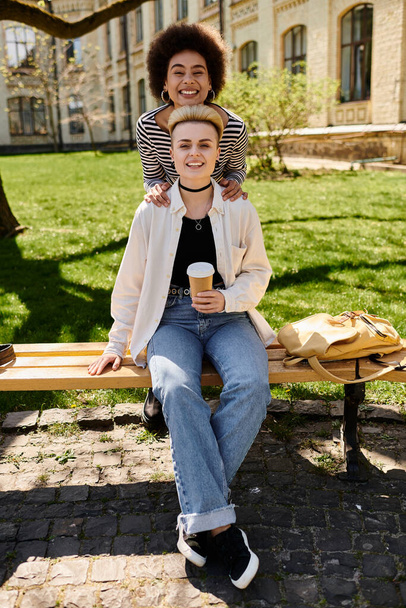 Twee jonge meisjes, vrienden, zitten samen op een bank in een vredig park, genieten van elkaars gezelschap op een zonnige dag.. - Foto, afbeelding