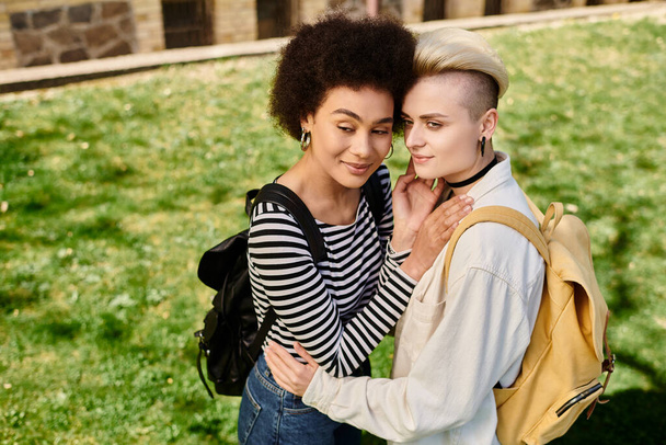 Due giovani donne, in abbigliamento casual, si abbracciano amorevolmente nel campo erboso, condividendo un momento di genuina connessione. - Foto, immagini