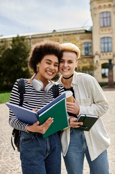 Két fiatal nő alkalmi ruhában, könyvekkel a kezében, egy egyetemi egyetem épülete előtt áll.. - Fotó, kép