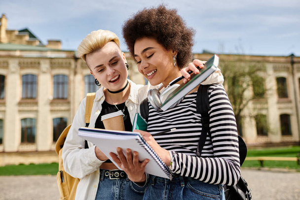 Két fiatal nő, elegánsan öltözve, elmerülve egy jegyzetfüzetben egy egyetemi egyetem épülete előtt.. - Fotó, kép