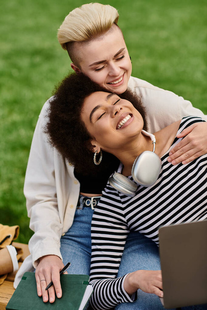 Twee jonge vrouwen zitten op gras met een laptop, genieten van het buitenleven tijdens het werken of studeren samen. - Foto, afbeelding