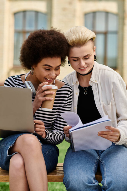Duas meninas em traje casual sentado em um banco, trabalhando em um laptop e tomando café em um ambiente aconchegante ao ar livre. - Foto, Imagem