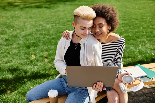 Deux jeunes femmes, assises sur un banc, englouties dans un écran d'ordinateur portable, travaillant ou étudiant éventuellement ensemble. - Photo, image
