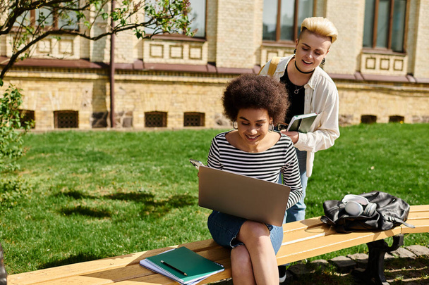 Due studenti, assorbiti dal loro lavoro, si siedono su una panchina con un computer portatile. - Foto, immagini