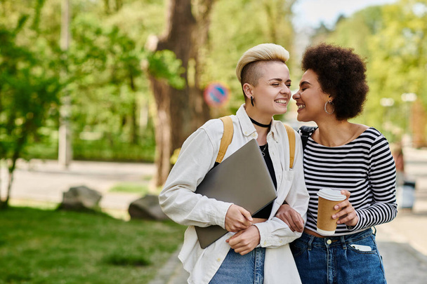 Δύο νεαρές γυναίκες με περιστασιακή ενδυμασία συνομιλούν σε ένα σκηνικό πάρκου, συνδέοντας η μία την άλλη σε ένα ήσυχο εξωτερικό περιβάλλον κοντά σε πανεπιστημιούπολη. - Φωτογραφία, εικόνα