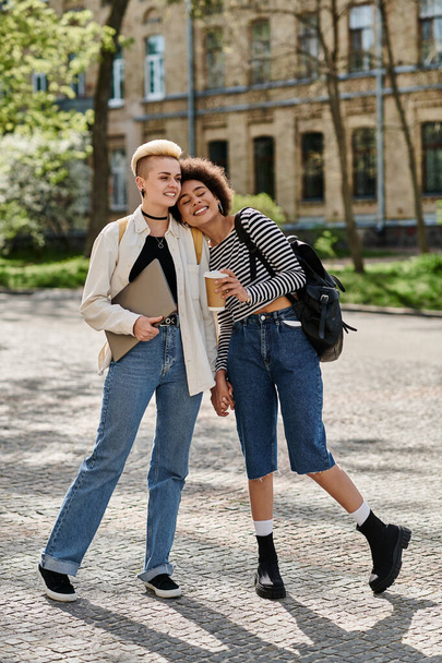 Wielokulturowa para lesbijek w modnych strojach, spacerująca w pobliżu kampusu uniwersyteckiego. - Zdjęcie, obraz