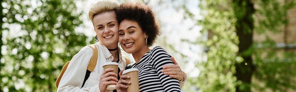 Δύο νεαρές γυναίκες, πολυπολιτισμικό λεσβιακό ζευγάρι, αγκαλιάζονται θερμά σε ένα πάρκο, εκφράζοντας την αγάπη και τη σύνδεση. - Φωτογραφία, εικόνα