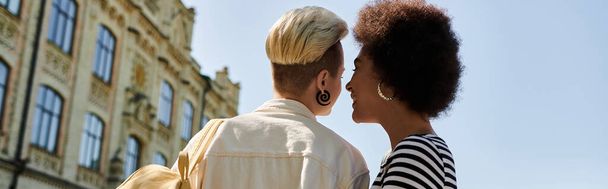 Due eleganti donne nere condividono un tenero bacio di fronte a un edificio universitario, mostrando amore e diversità.. - Foto, immagini