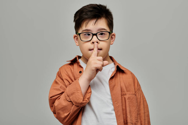 Мальчик с синдромом Дауна в очках делает знак молчания. - Фото, изображение