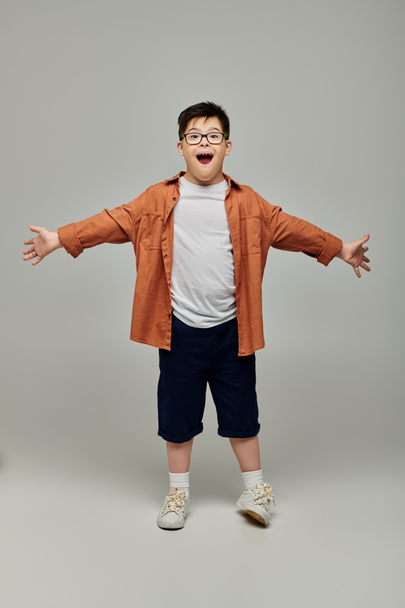 menino com síndrome de Down, braços estendidos, contra fundo cinza. - Foto, Imagem