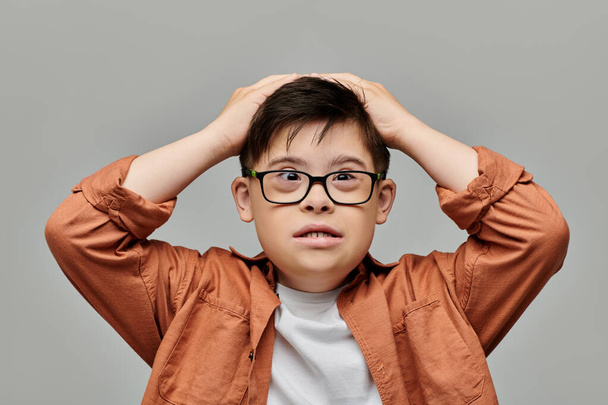 Un bambino con la sindrome di Down con gli occhiali sta tenendo la testa in contemplazione. - Foto, immagini