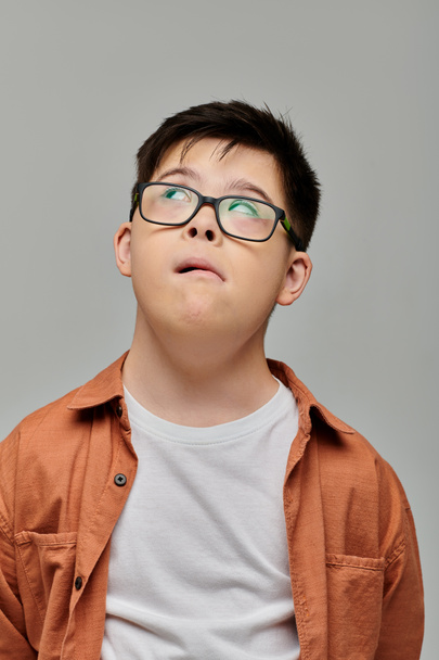 Un niño pequeño con síndrome de Down con gafas mira hacia arriba, su expresión curiosa y atractiva. - Foto, imagen