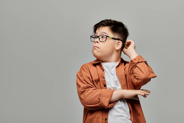Un animado niño con síndrome de Down con gafas posa sobre un fondo gris. - Foto, Imagen