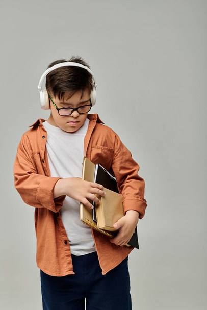 μικρό αγόρι με σύνδρομο Down φοράει ακουστικά ενώ κρατά βιβλία. - Φωτογραφία, εικόνα
