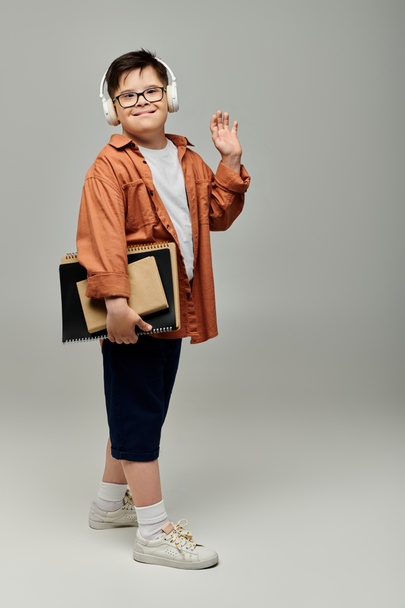 mały chłopiec z zespołem Downa, noszący słuchawki, trzymający książki.. - Zdjęcie, obraz
