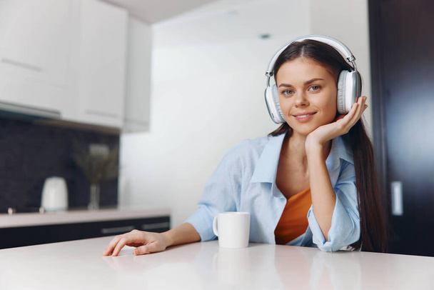 Mladá žena těší hudbu se sluchátky, zatímco v kuchyni doma, pocit uvolněnosti a pobavení - Fotografie, Obrázek