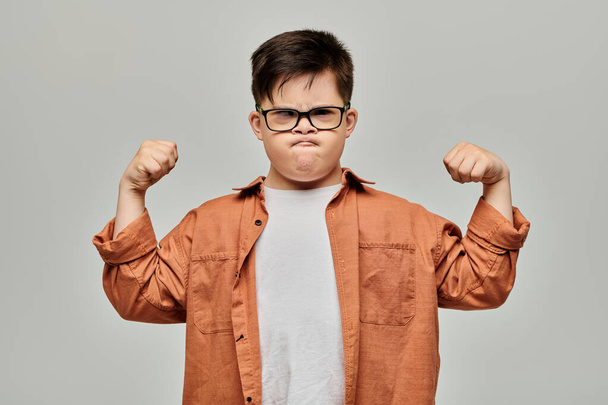 Mały chłopiec z zespołem Downa w okularach napina mięśnie, pokazując swoją siłę i determinację. - Zdjęcie, obraz