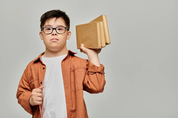 Мальчик с синдромом Дауна держит стопку книг. - Фото, изображение