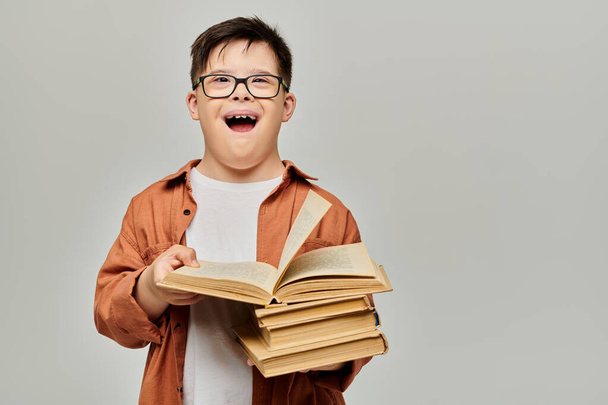 Мальчик с синдромом Дауна в очках весело держит в руках большую стопку книг. - Фото, изображение