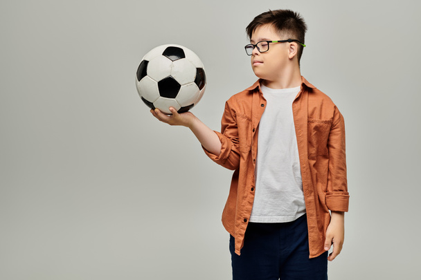niño pequeño con síndrome de Down con gafas sosteniendo una pelota de fútbol. - Foto, imagen