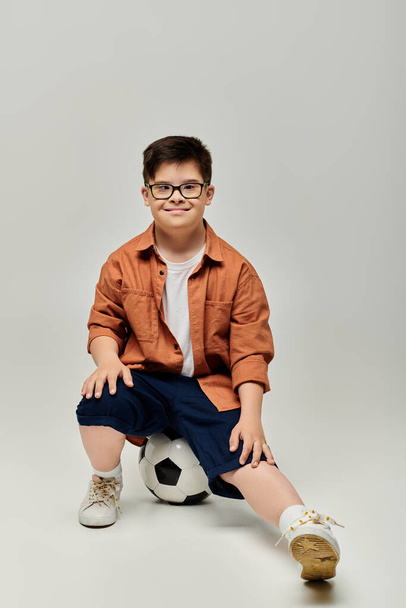 Słodki chłopiec z zespołem Downa w okularach pozujących z piłką nożną. - Zdjęcie, obraz