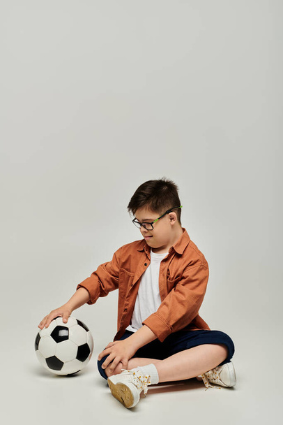 サッカーボールと床に座っているダウン症候群の小さな男の子. - 写真・画像