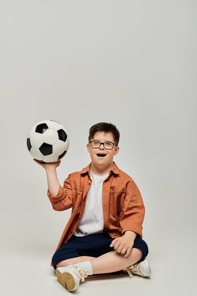 Ένα αγόρι με σύνδρομο Down κρατά μια μπάλα ποδοσφαίρου σε λευκό φόντο. - Φωτογραφία, εικόνα