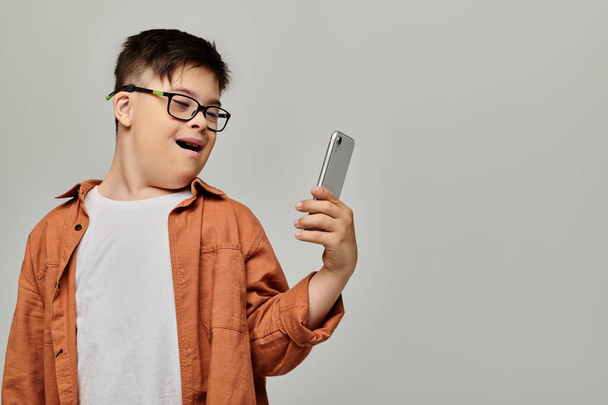 Ένα αγόρι με σύνδρομο Down με γυαλιά κρατά ένα κινητό τηλέφωνο. - Φωτογραφία, εικόνα