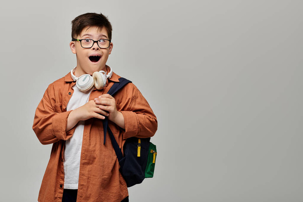 Mały chłopiec z zespołem Downa w okularach i plecakiem bada z ciekawością. - Zdjęcie, obraz