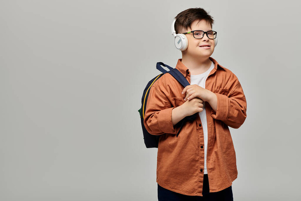 ヘッドフォンを着てバックパックを運ぶダウン症候群の小さな男の子. - 写真・画像