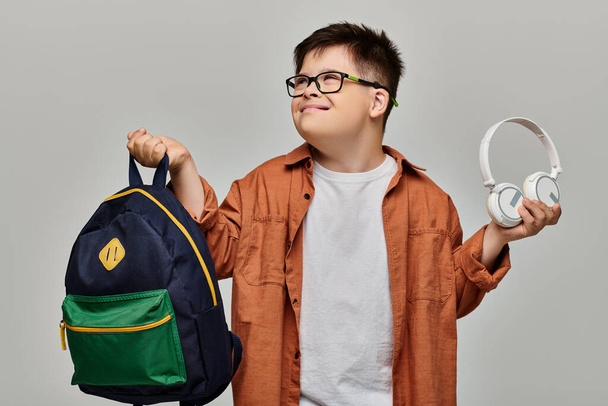 маленький хлопчик з синдромом Дауна тримає рюкзак і навушники. - Фото, зображення