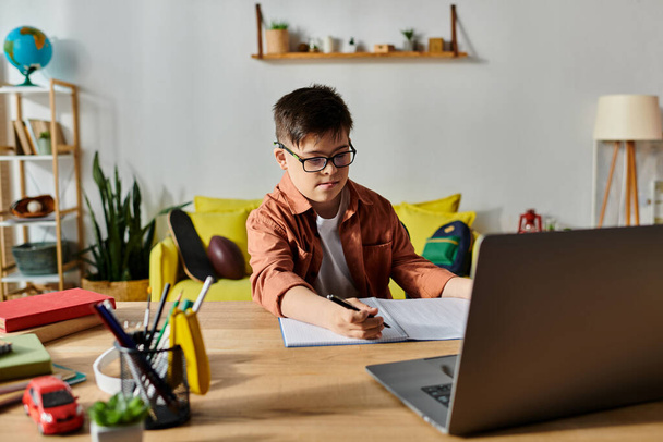 Een schattige jongen met Down syndroom gericht op zijn laptop thuis. - Foto, afbeelding