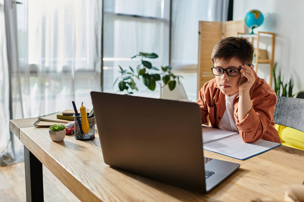 Ein Junge mit Down-Syndrom sitzt mit einem Laptop am Schreibtisch - Foto, Bild