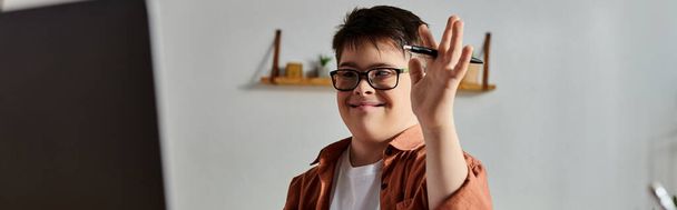 Boy with Down syndrome in glasses waves hand at computer screen. - Фото, изображение