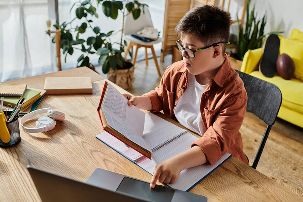 entzückender Junge mit Down-Syndrom vertieft in Laptop und Buch am Tisch. - Foto, Bild